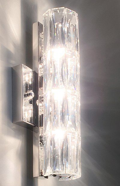 A wall light with a clear glass shade is lit up on a wall.
