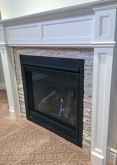 A fireplace with a white mantle and a brick wall in a living room.