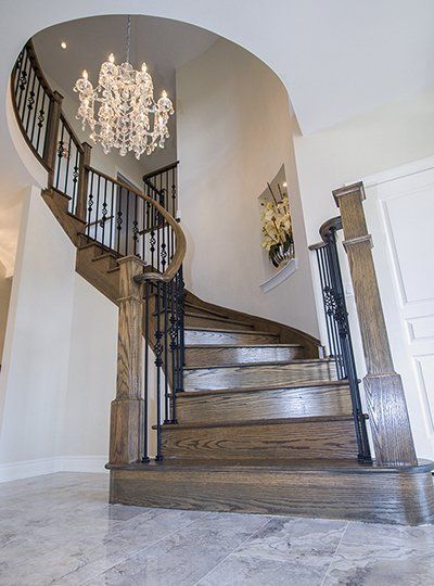A wooden spiral staircase with a chandelier hanging from the ceiling.