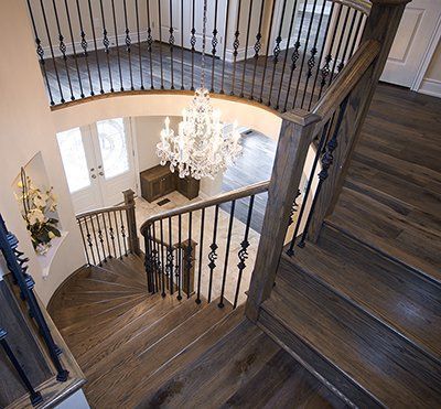 A wooden spiral staircase with a wrought iron railing and a chandelier hanging from the ceiling.