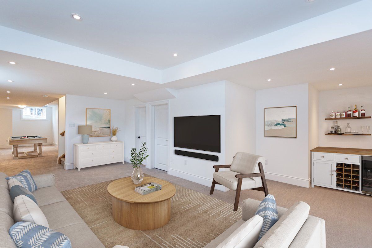 A finished basement with a living area: sofa, armchair, TV, bar, and carpeted flooring.
