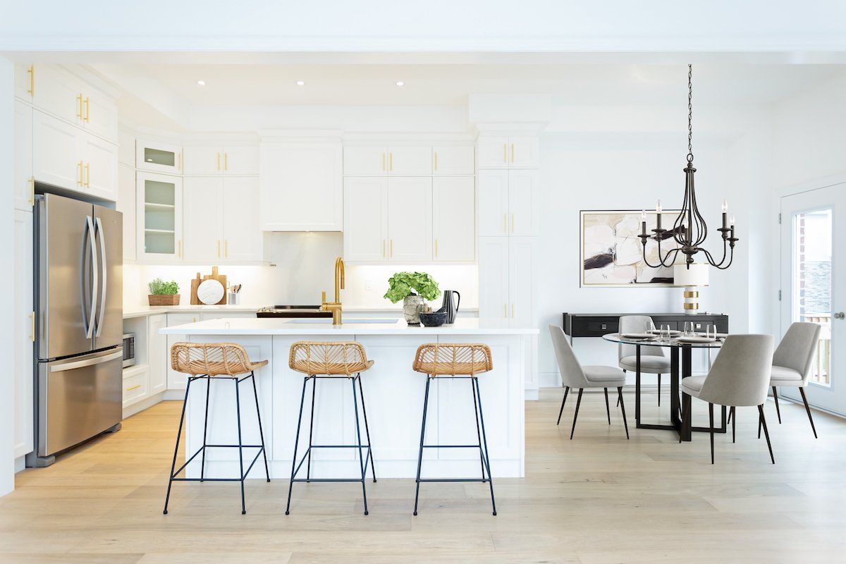 A kitchen with white cabinets , stainless steel appliances , a refrigerator , a table and chairs.