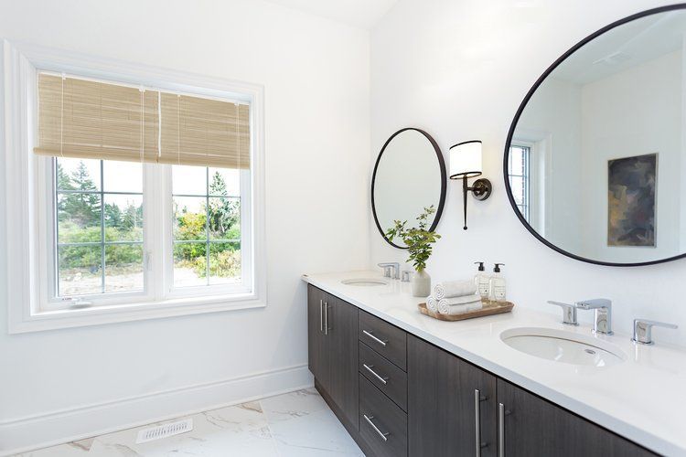 A bathroom with two sinks , two mirrors and a window.