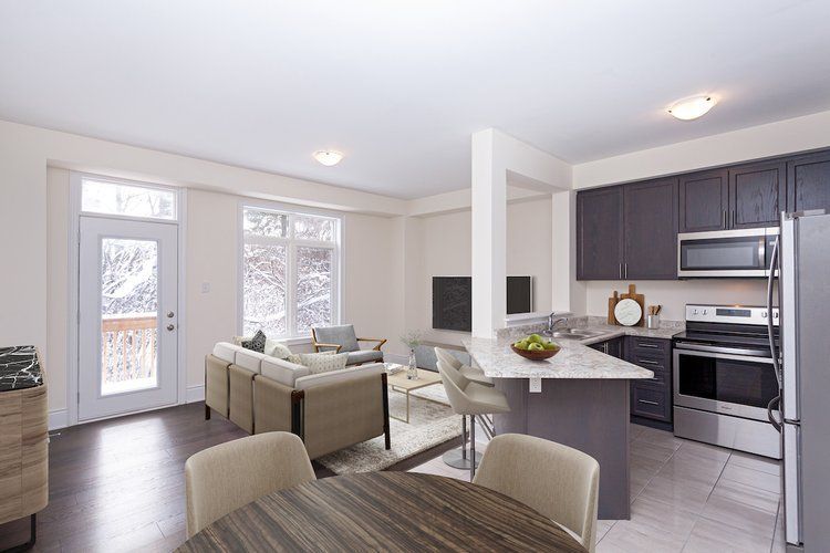 A living room with a table and chairs and a kitchen with stainless steel appliances.
