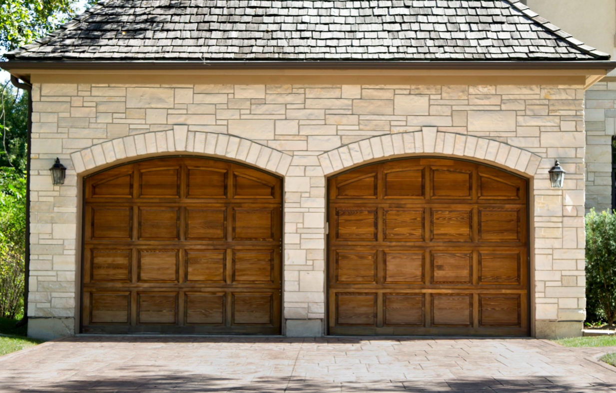 A stone garage with wooden garage doors and a roof.