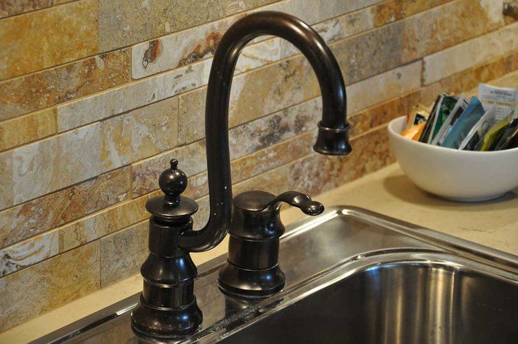 A kitchen sink with a black faucet and a bowl of tea in the background.