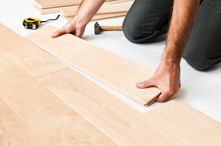 A man is kneeling down to install a wooden floor.