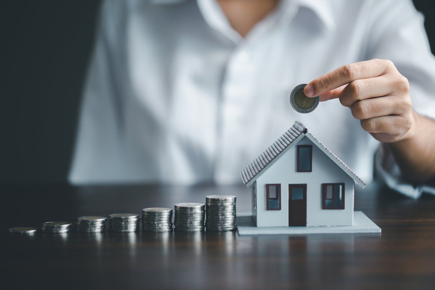 A person is putting a coin on top of a model house.