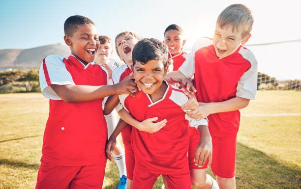 A group of young boys are hugging each other on a soccer field.