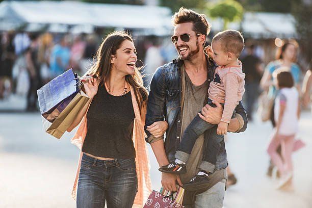 A man is holding a baby while a woman holds shopping bags.