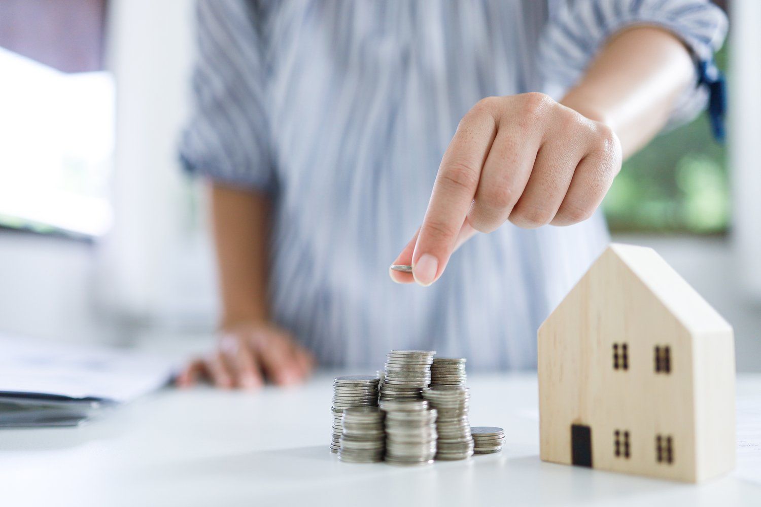 A person is stacking coins next to a model house.