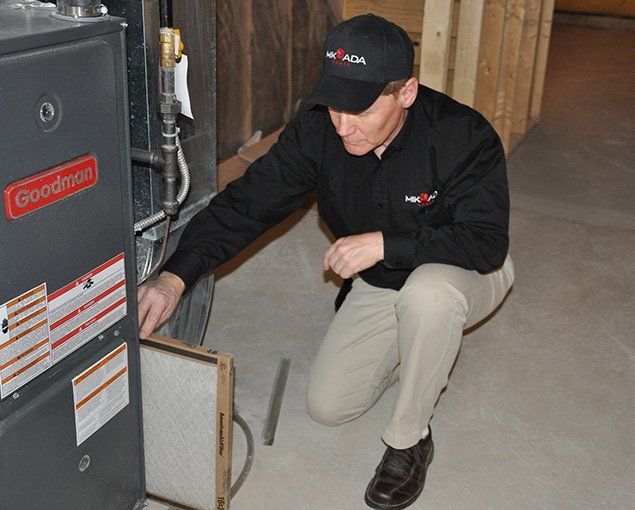 A man is kneeling down next to a goodman air conditioner