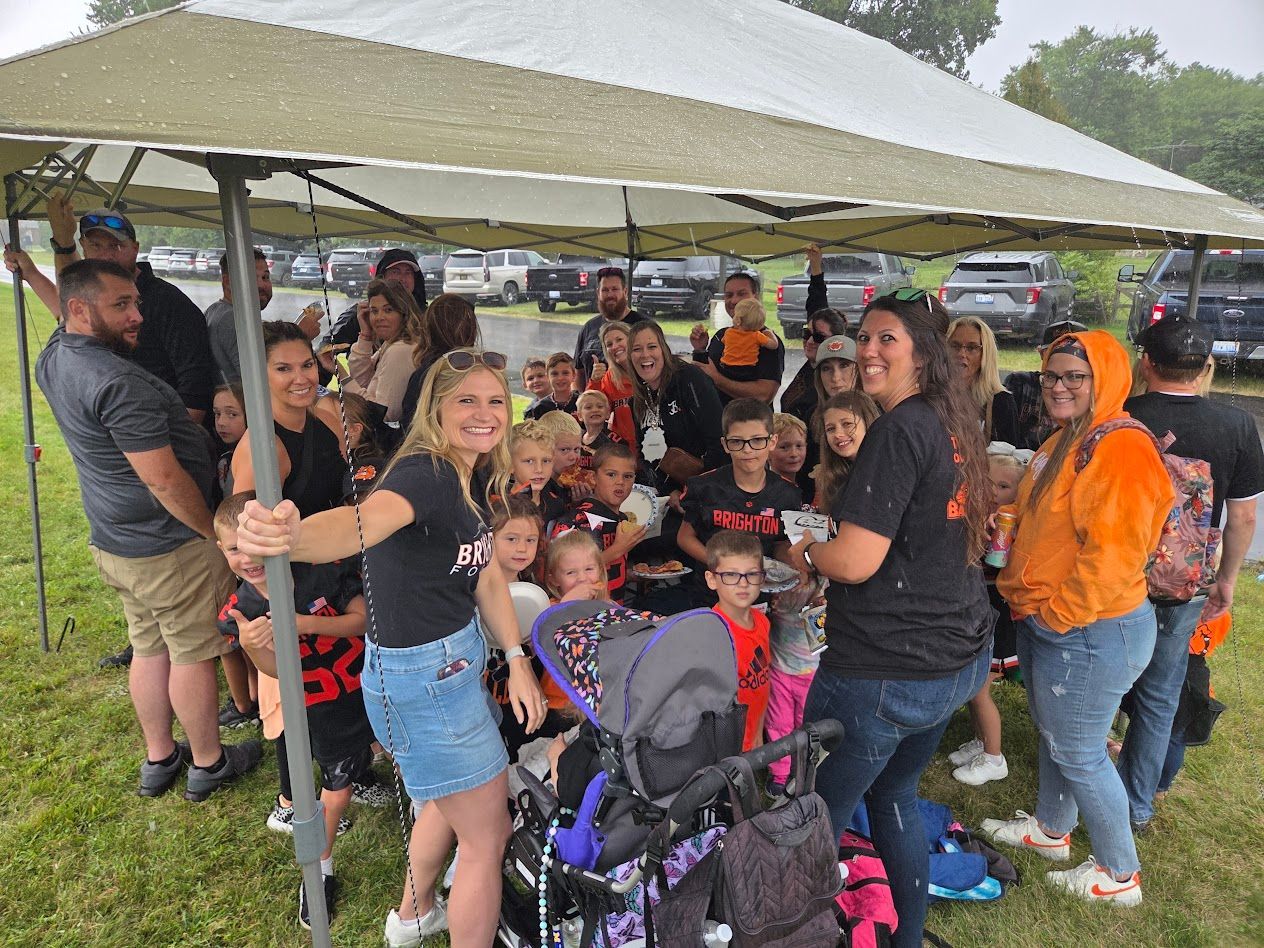 Group of people gathered under a canopy at an outdoor event, posing around a stroller in the rain.