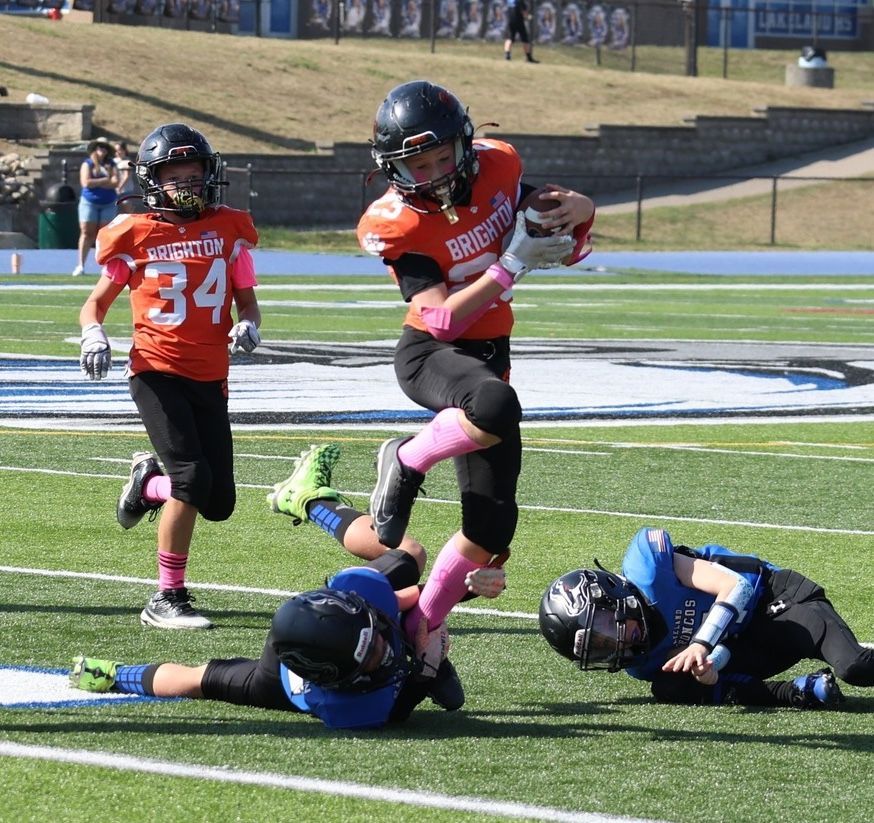 Youth football players in orange and blue tackle on a grassy field during a game