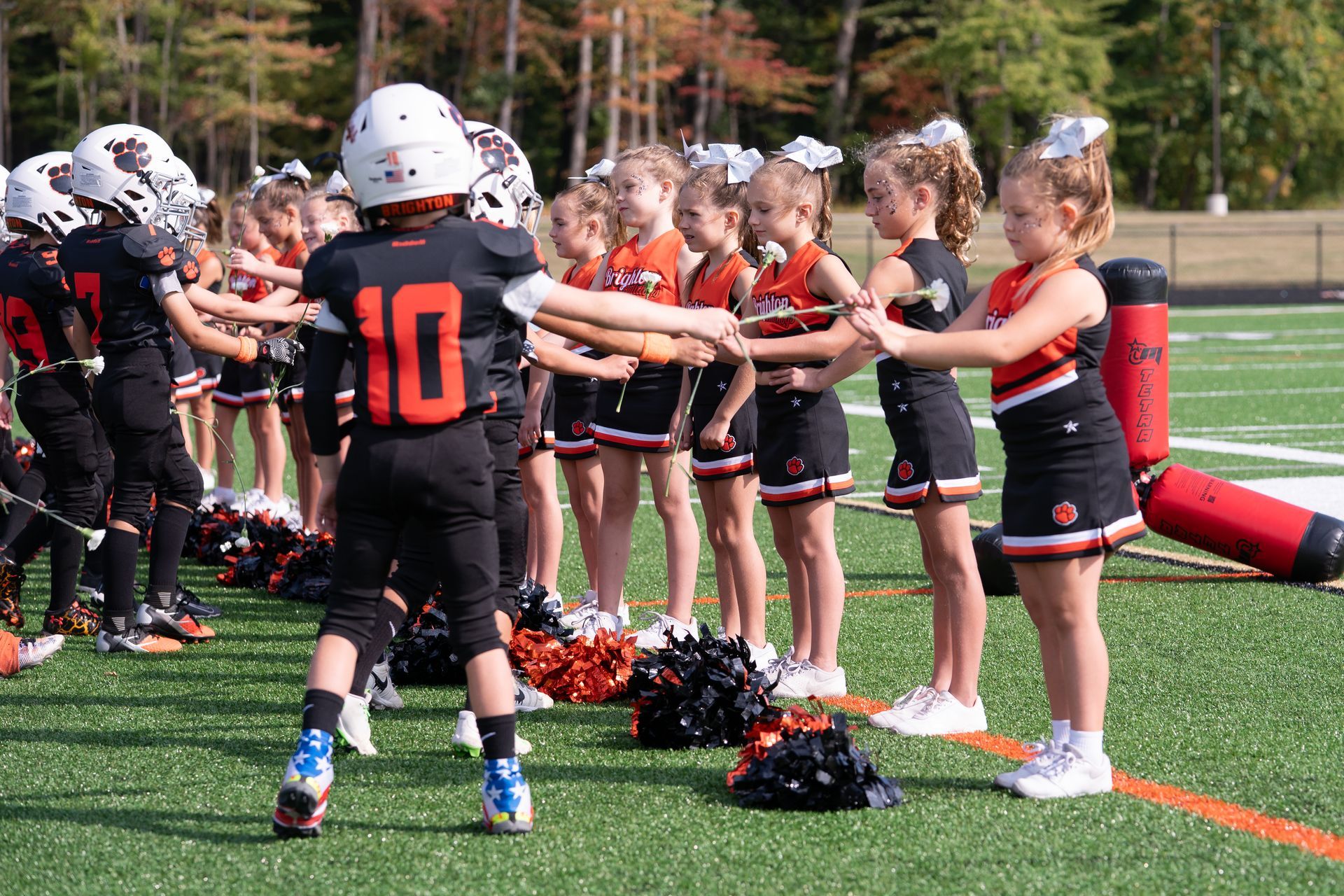 Youth football players high-fiving in two lines on a turf field, with pom-poms and cones nearby