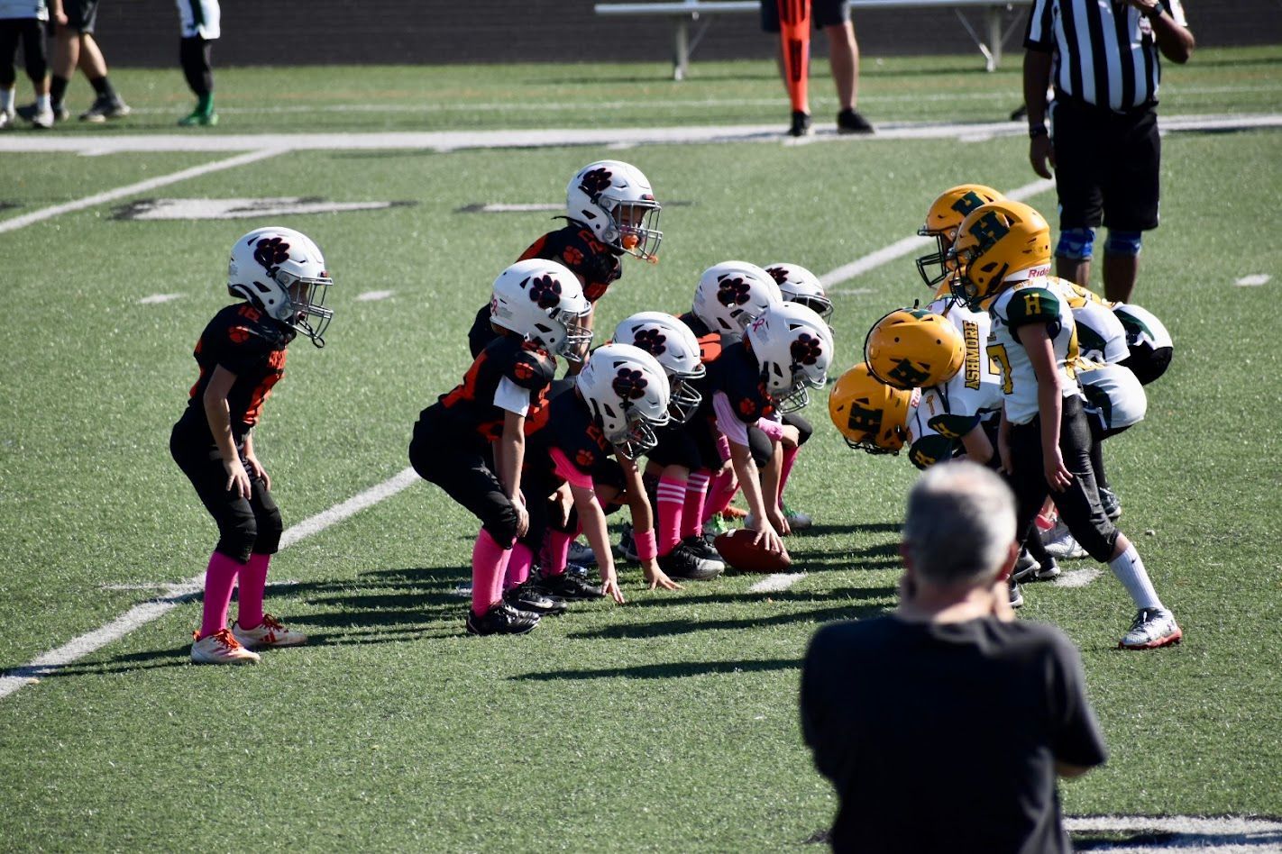 Youth football teams lined up at the line of scrimmage on a field, preparing for the snap.
