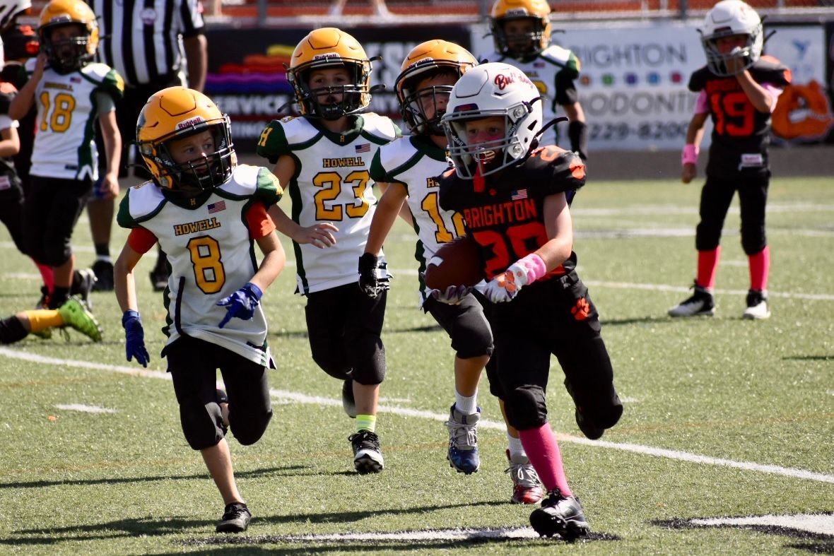 Youth football players in yellow and black uniforms running on a turf field during a game