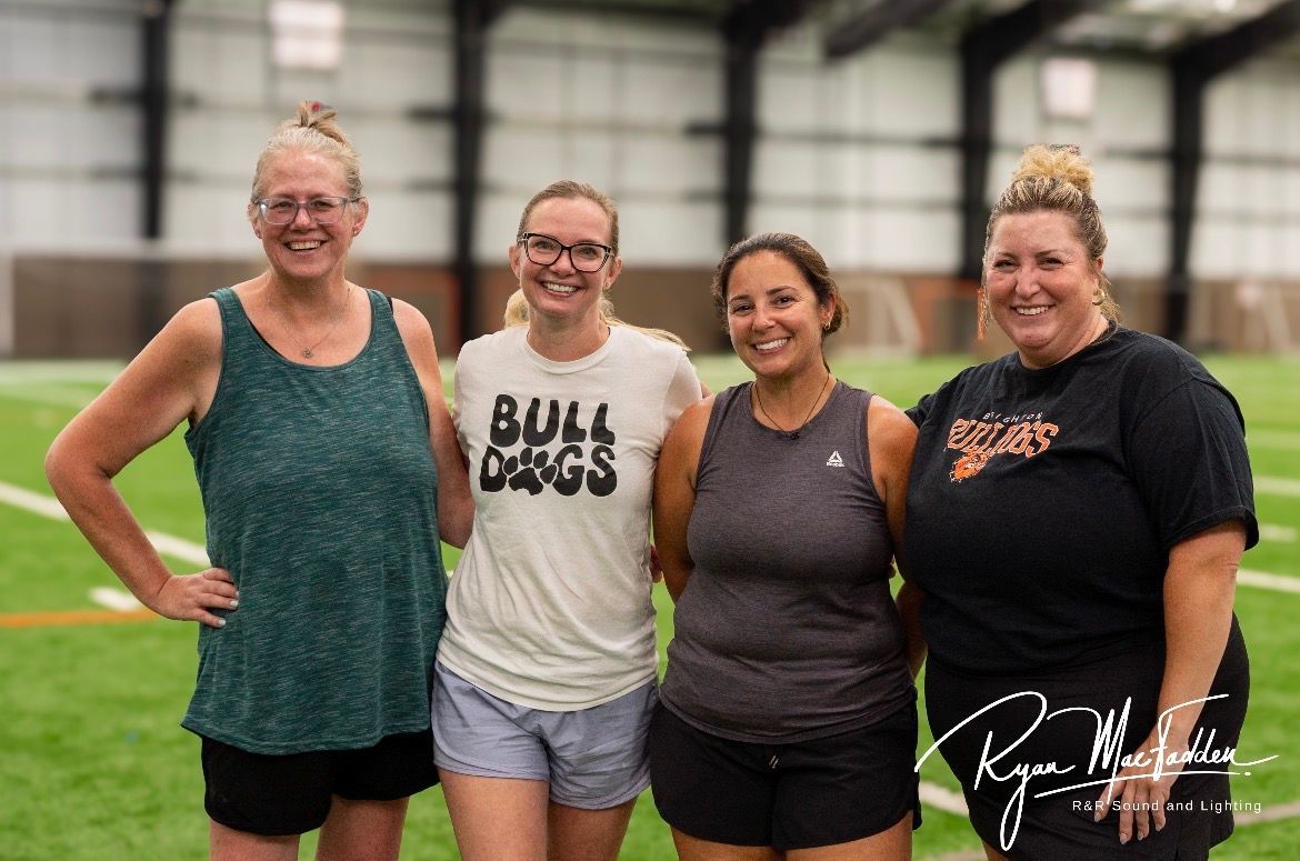 Four people posing indoors on a sports field, smiling in athletic wear