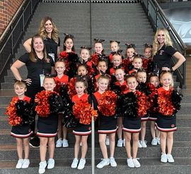 Cheer squad posing on indoor stairs in black, red, and orange uniforms