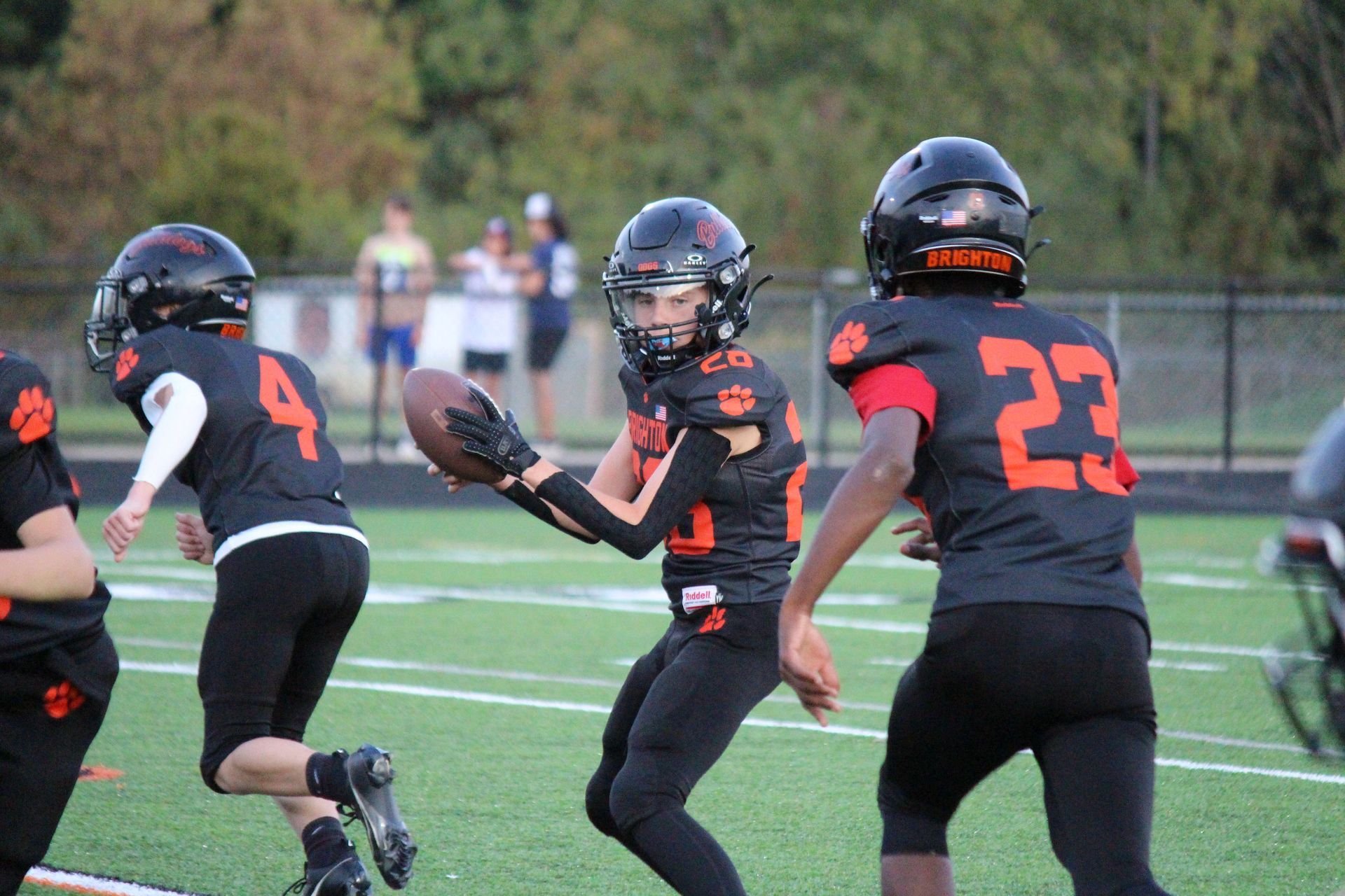 Youth football players in black uniforms prepare for a play on a grassy field.