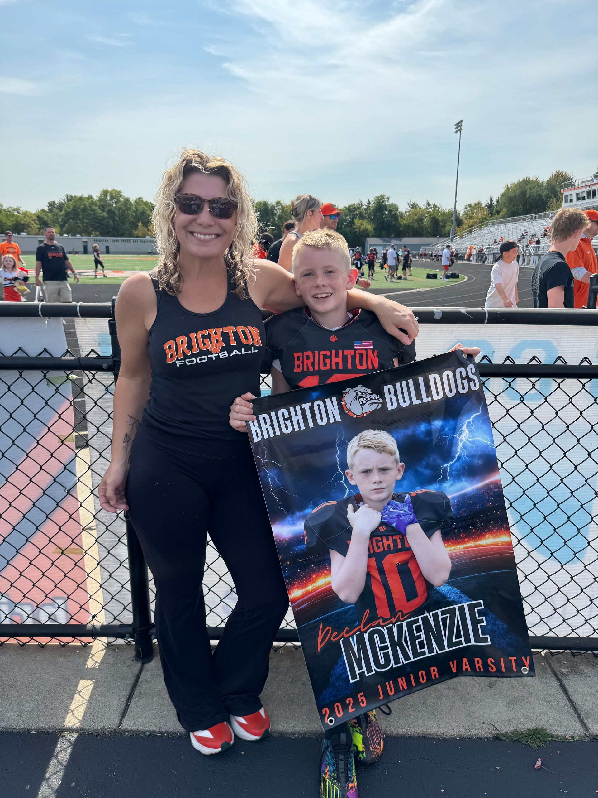 Two fans in black and orange posing at a track with a Dighton logo poster and a performer photo.