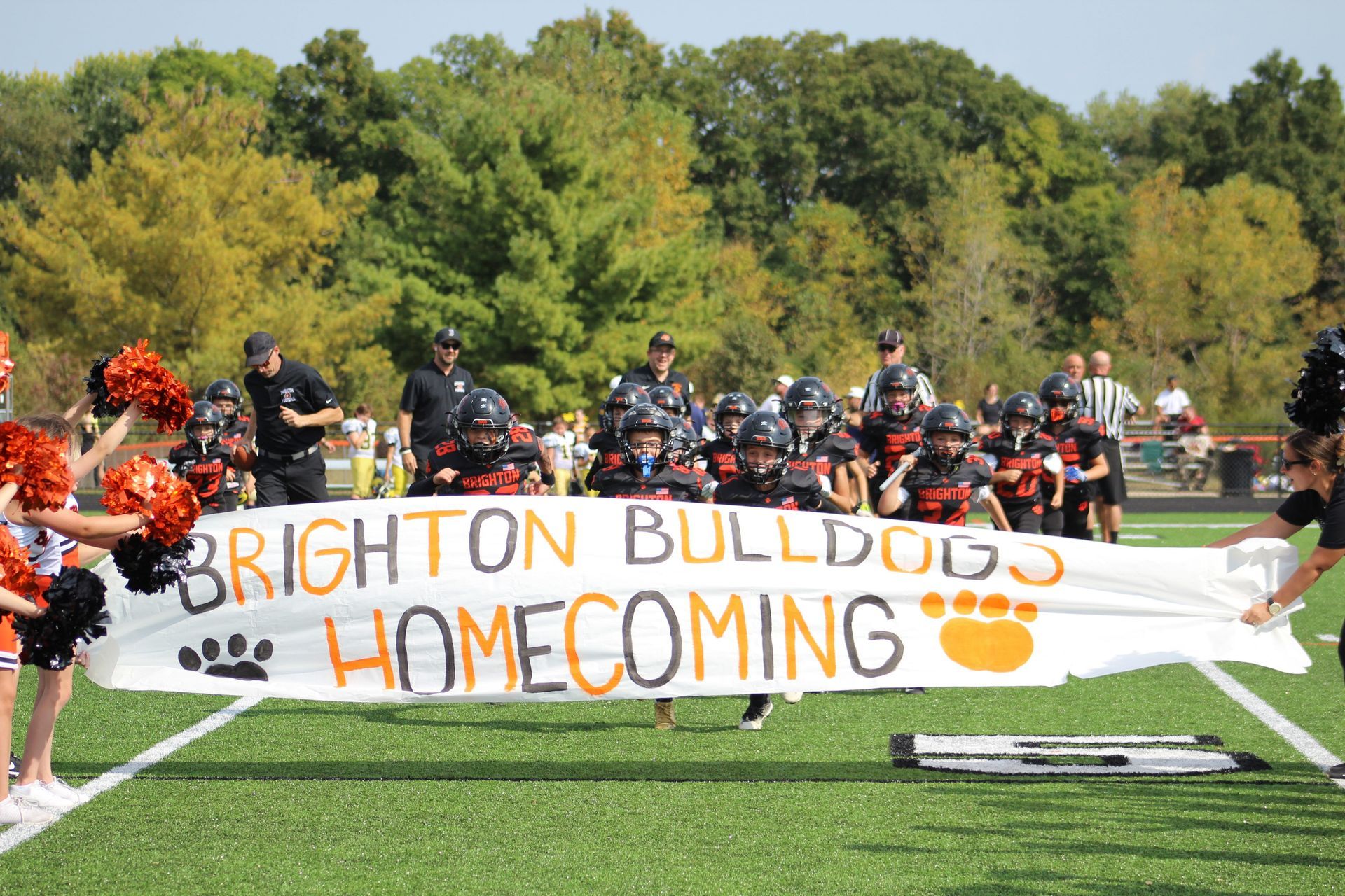Brighton Bulldogs homecoming banner held on a football field with players and cheerleaders behind it