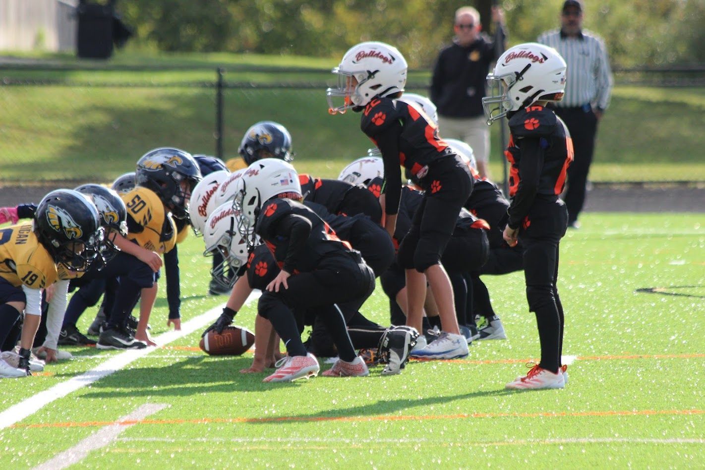 Youth football players line up at the line of scrimmage on a sunny field.