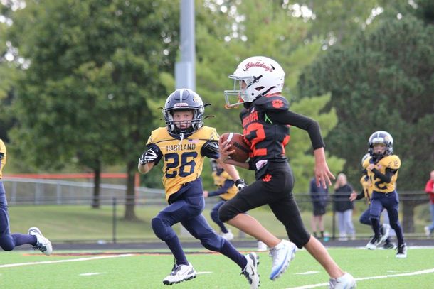 Youth football players run on a field, one in yellow chasing a black-and-red runner with the ball.
