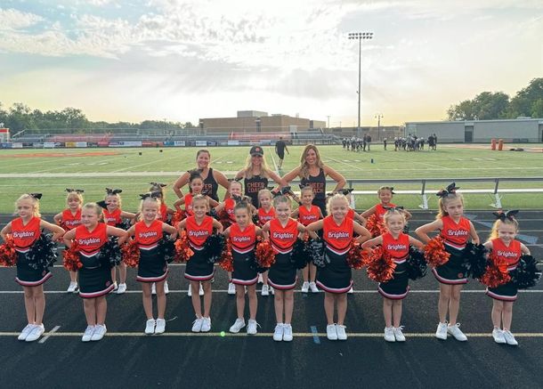 Cheer squad in red and black uniforms posing on a football field at sunset