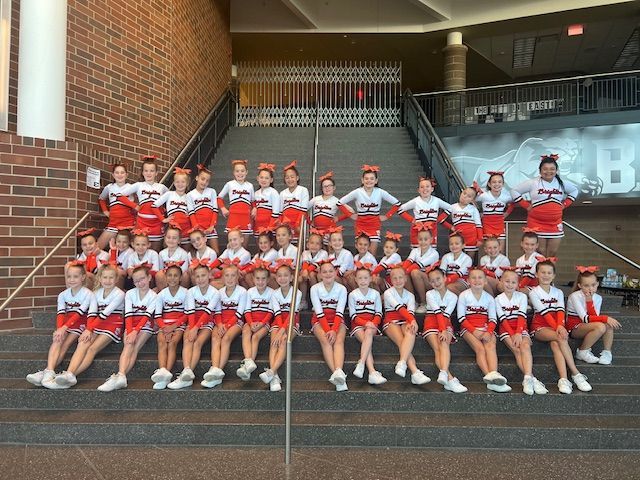 Cheer squad in red and white uniforms posing on steps inside a stadium or arena