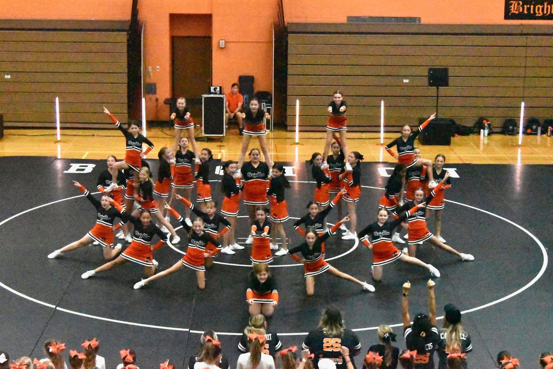 Cheerleading squad in orange uniforms performing a synchronized routine on an indoor gym floor
