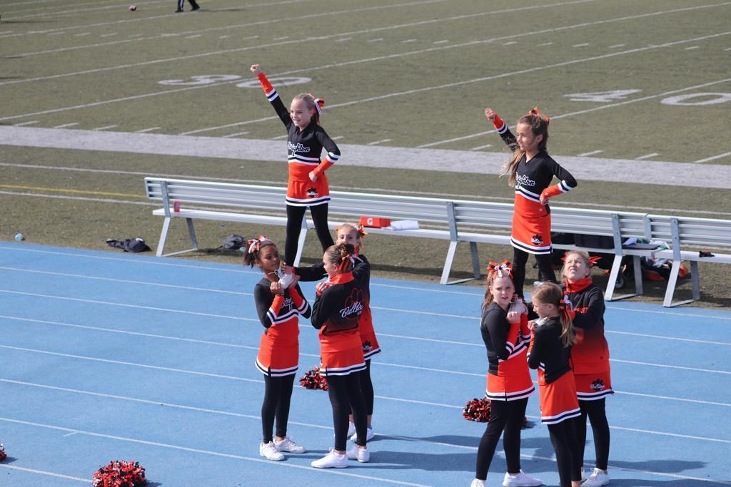Cheerleaders in orange and black uniforms performing on a blue track field at a sports stadium