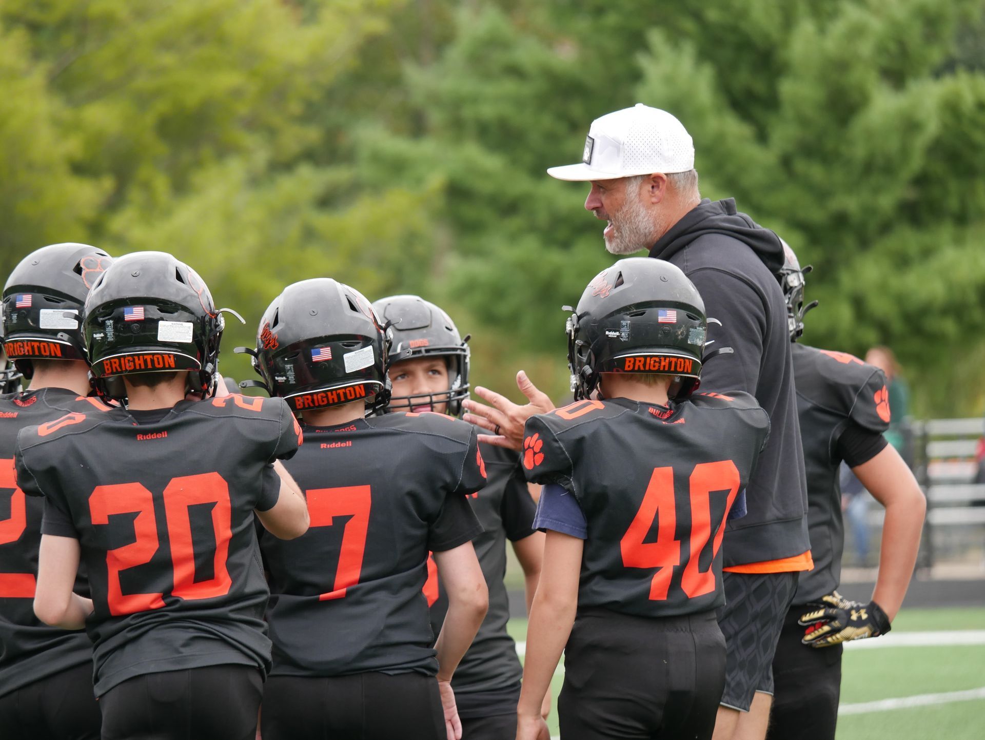 Football coach addressing helmeted players on the sideline during practice