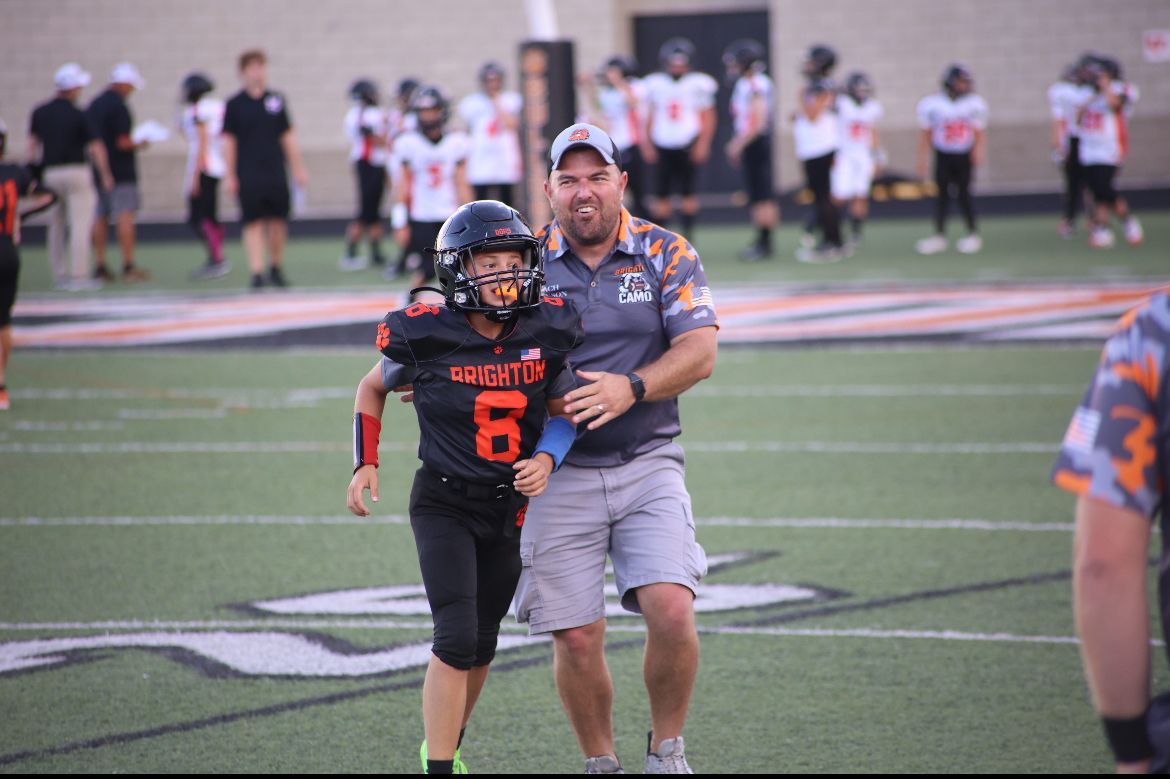 Football player in black and orange walks beside a coach on a field during practice