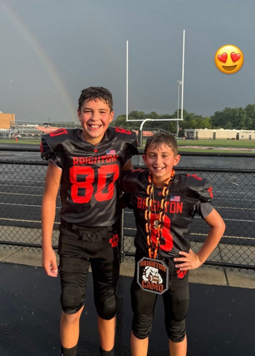 Two football players in black uniforms smiling on a track, with rainbow and heart-eyes emojis nearby.
