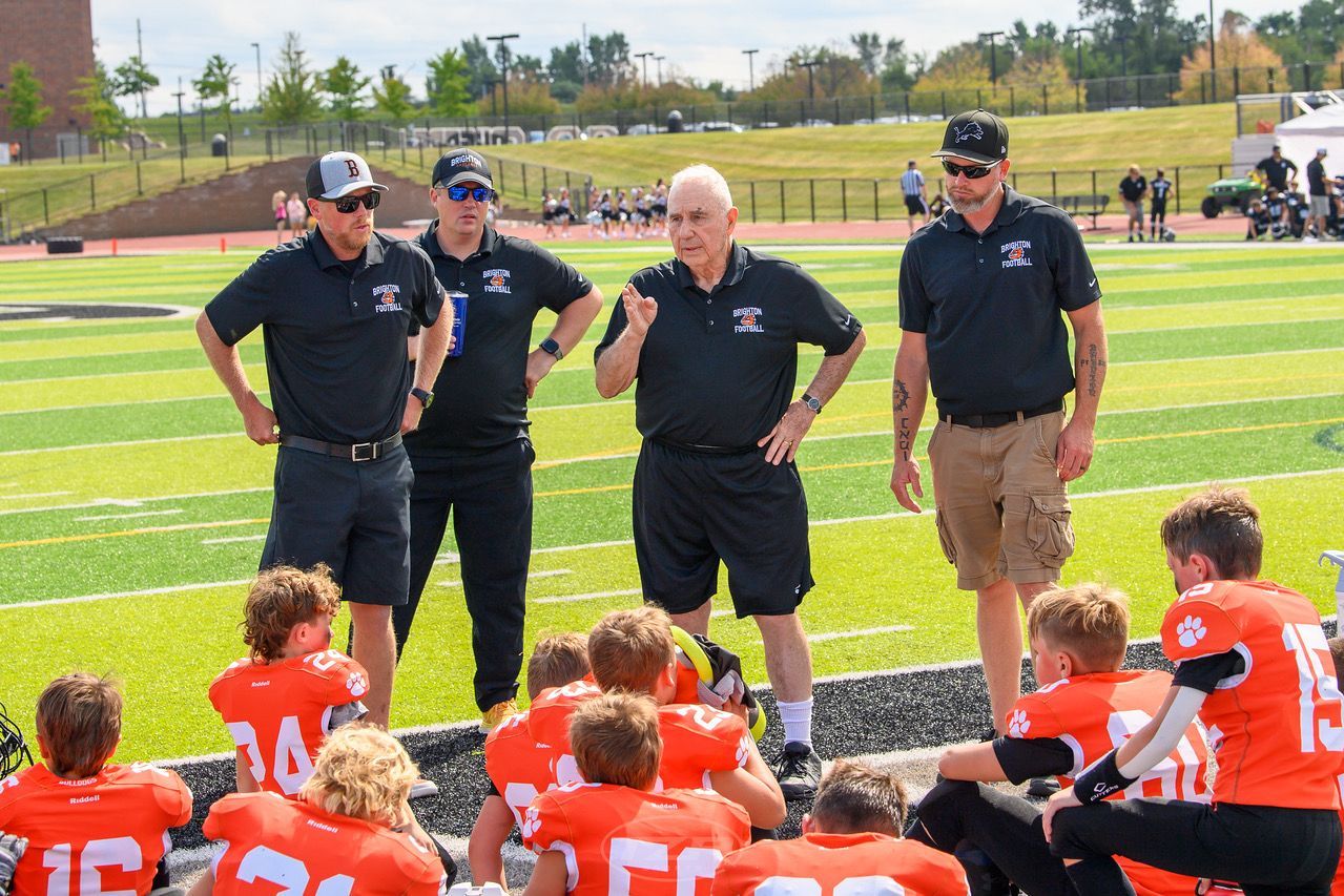 Football coaches addressing players on the field during a practice huddle.
