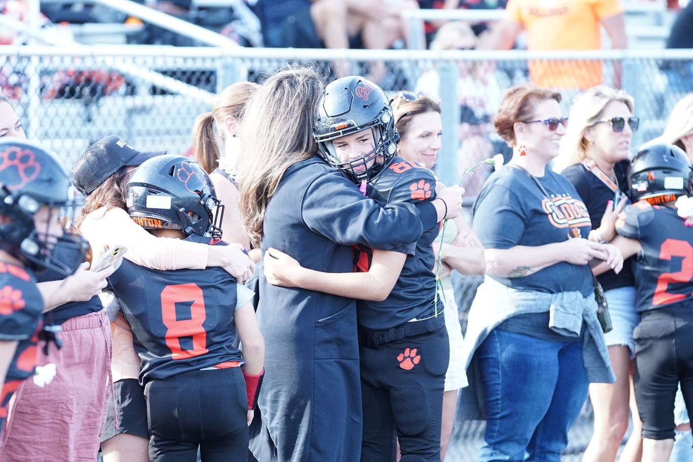 Football players and fans celebrate on the sideline in black and orange uniforms.