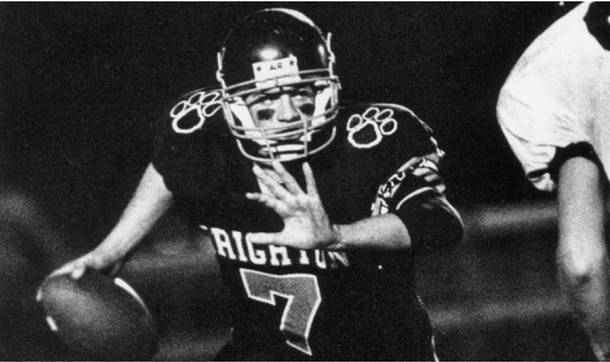 Black-and-white football player in a helmet, holding the ball and reaching forward during a play