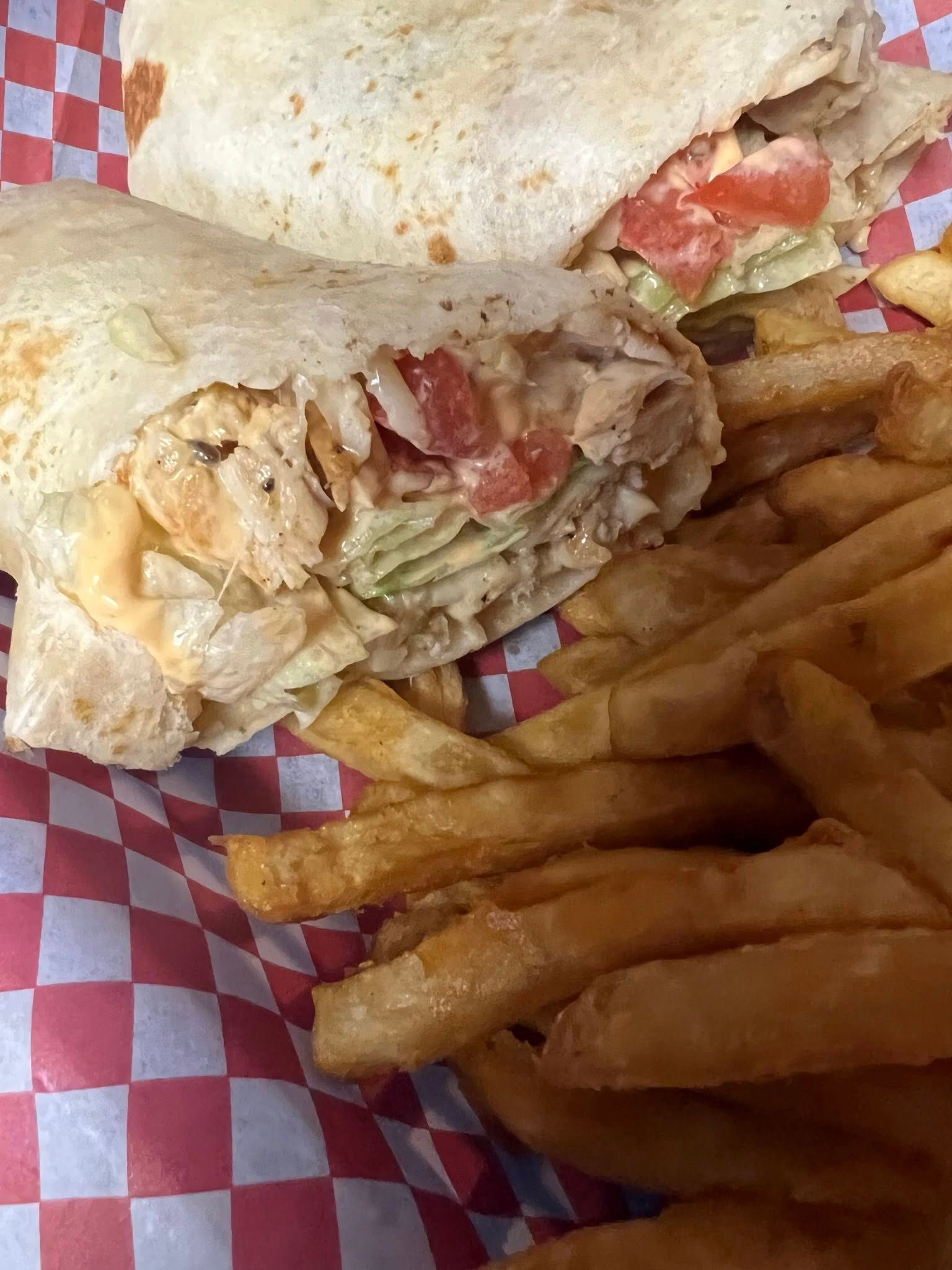 Chicken wrap and fries on red checkered paper basket lining.