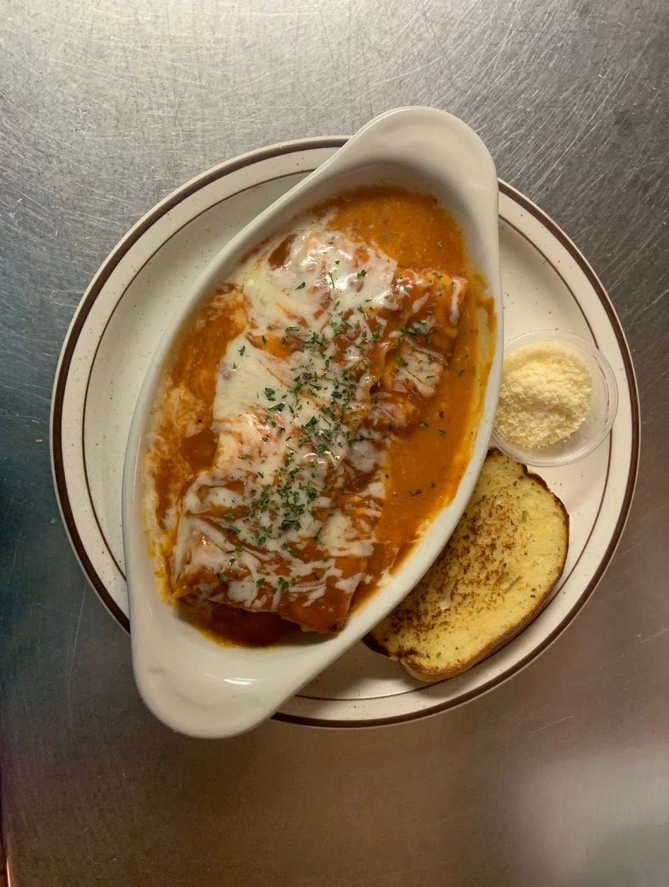 Baked pasta in red sauce with melted cheese, served with bread and butter on a plate.