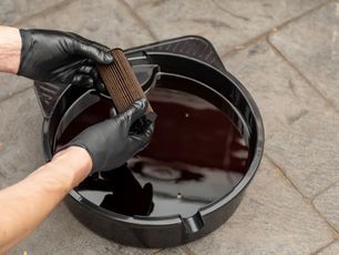 Person wearing black gloves holding an oil filter over a tray of used oil.