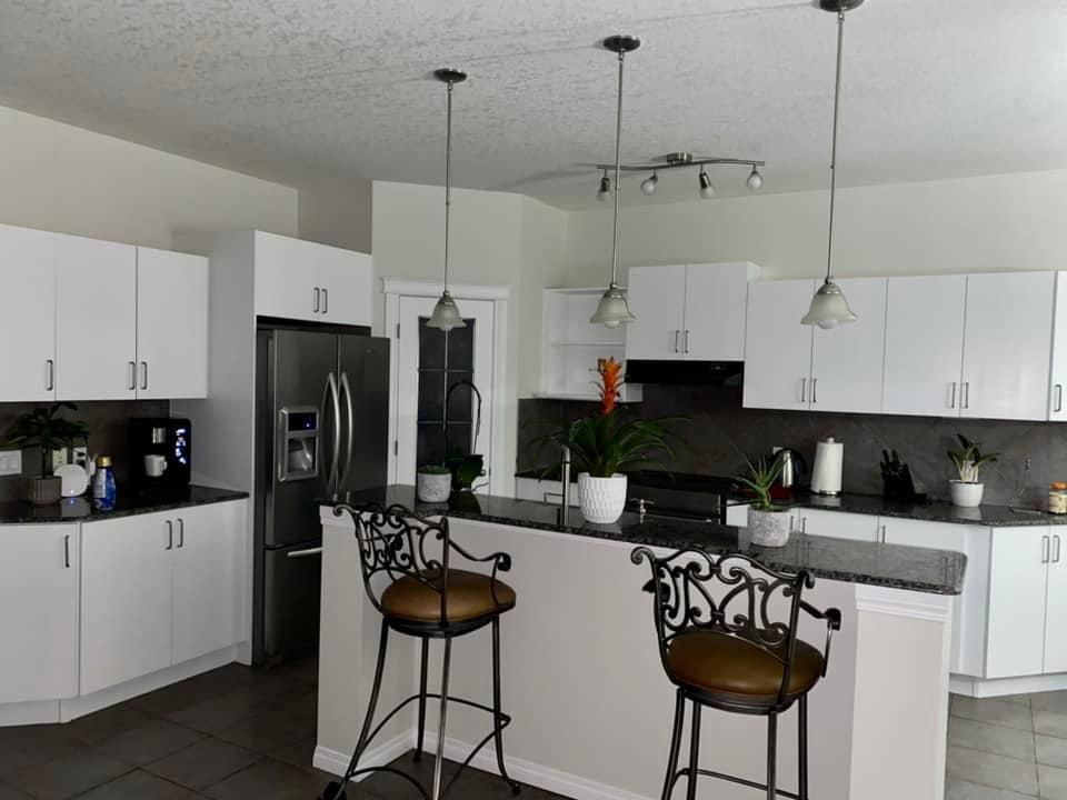 A kitchen with white cabinets , stools , a refrigerator and a sink.