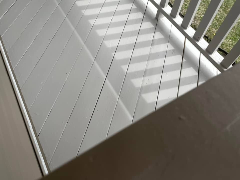 A white railing casts a shadow on a wooden deck