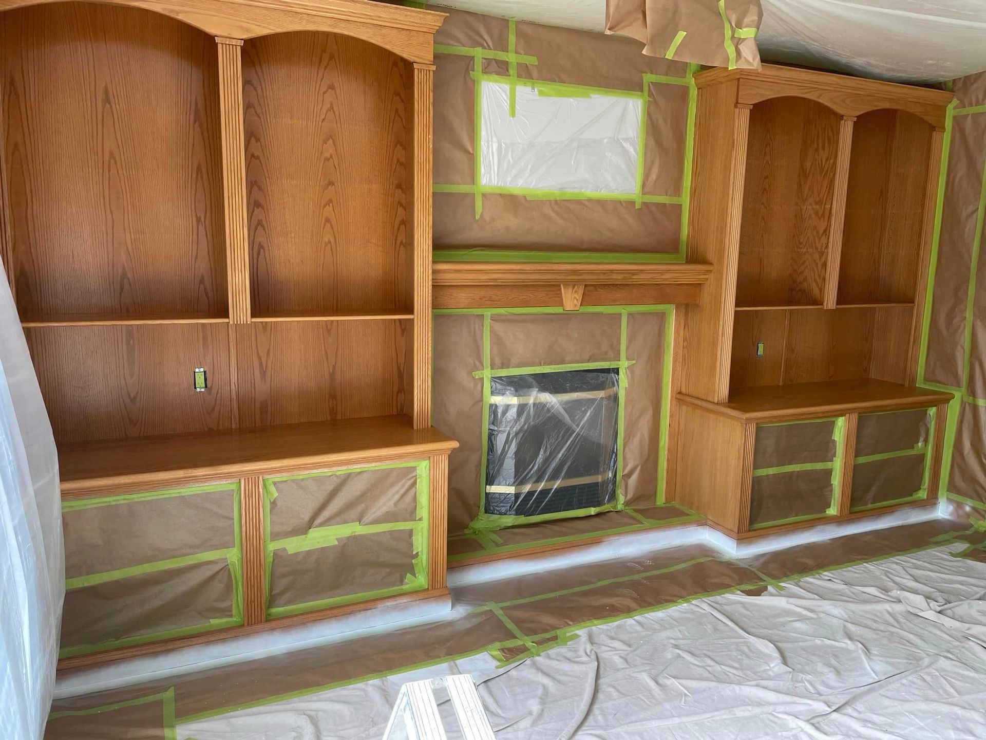 A living room with a fireplace and shelves is being painted.