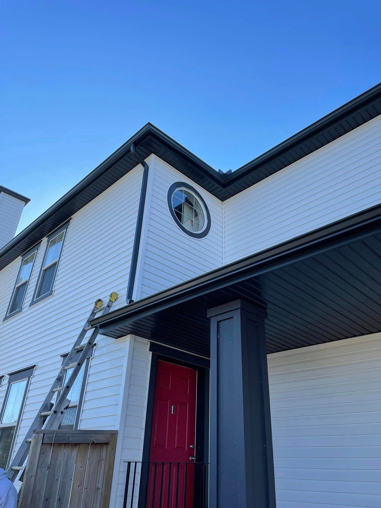 A white house with a red door and a ladder on the side of it.