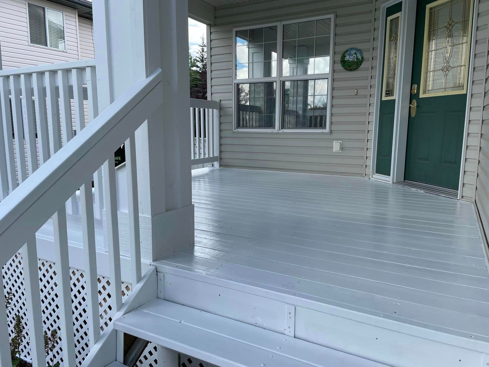 A white porch with stairs leading up to it and a green door.