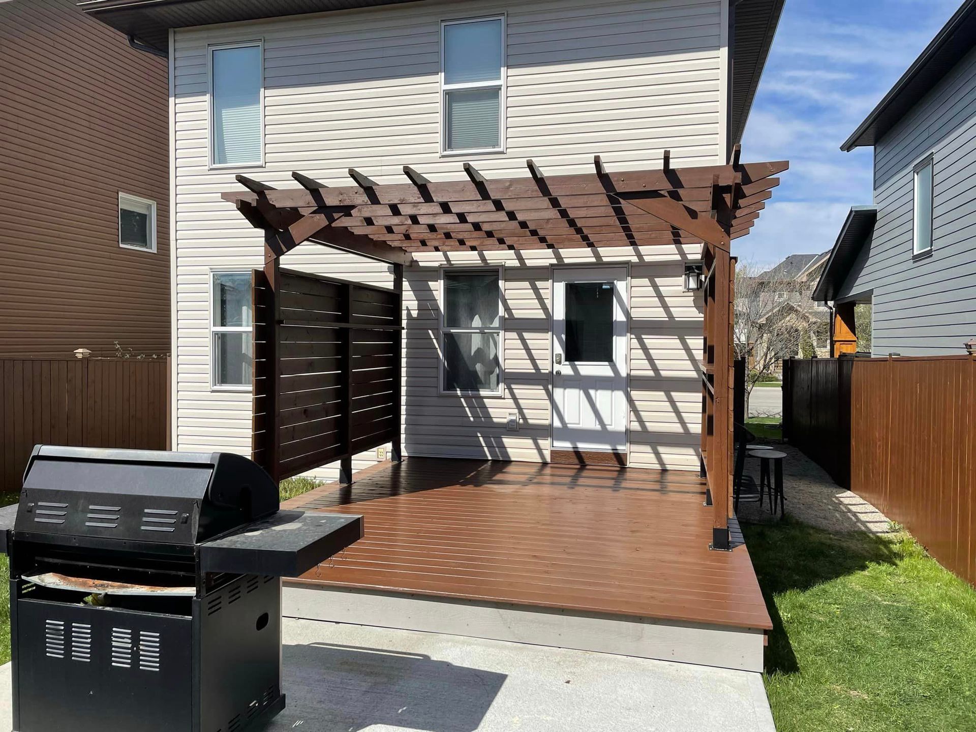 A house with a pergola and a grill in front of it.