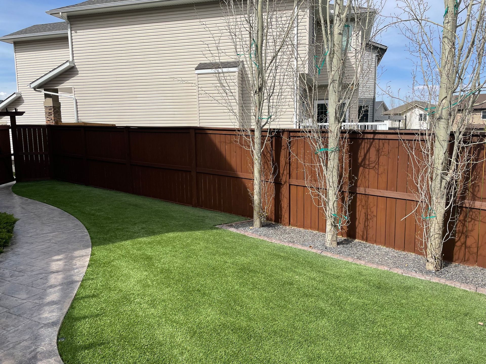 A wooden fence surrounds a lush green lawn in front of a house.
