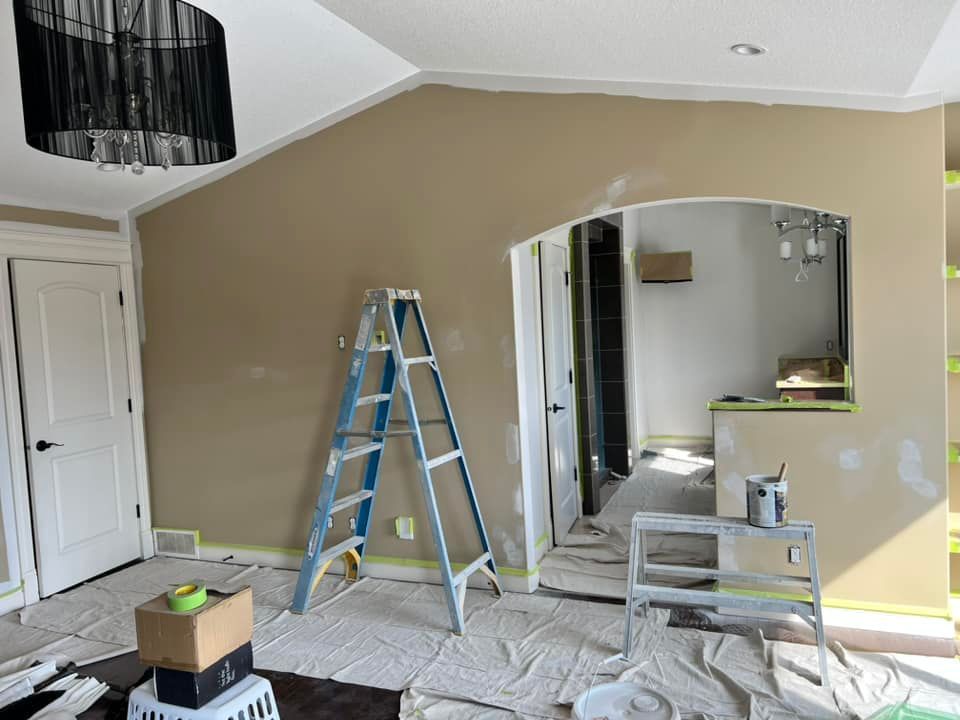 A living room is being painted with a ladder in the middle of the room.