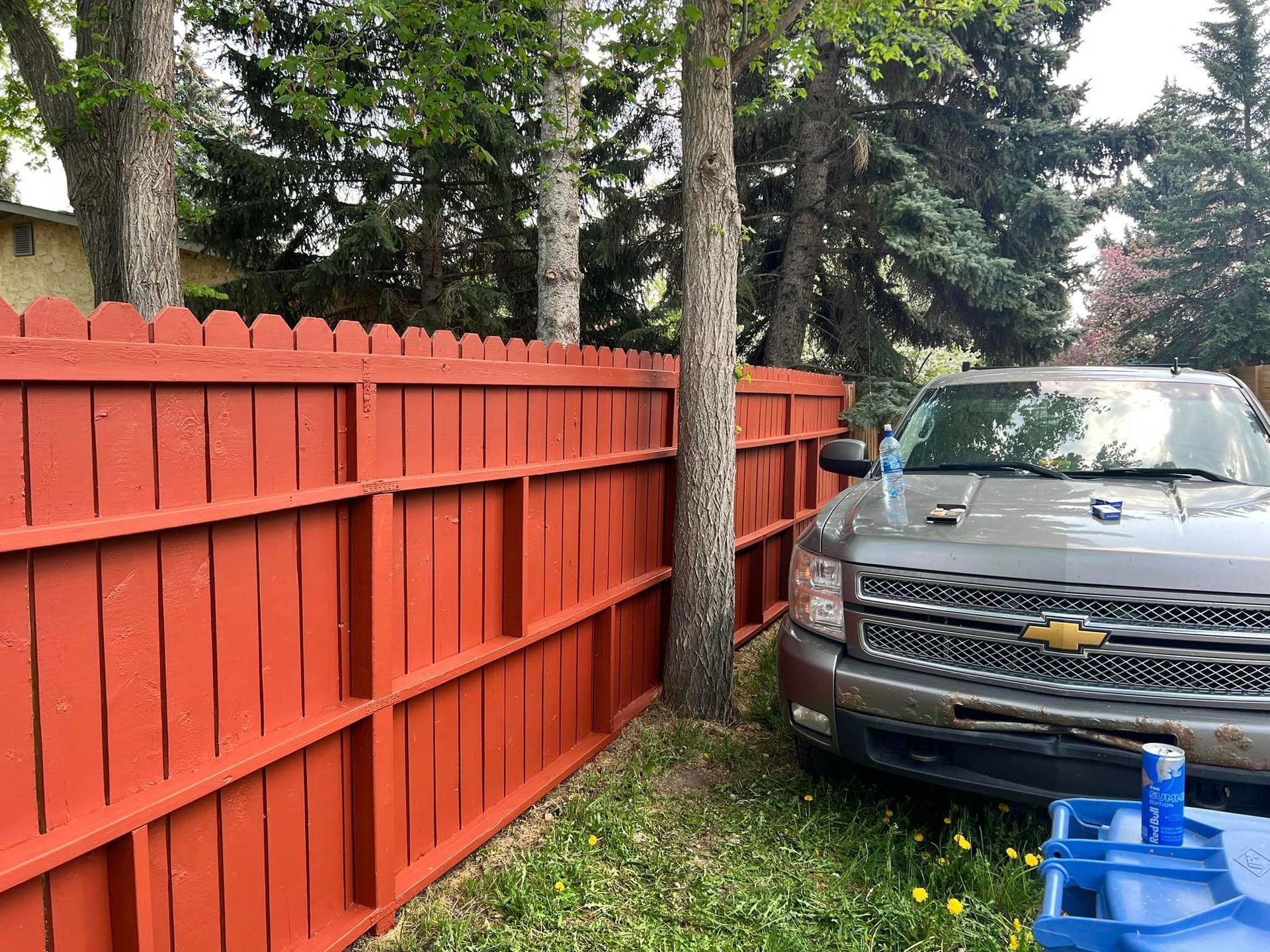 A gray truck is parked next to a red wooden fence.
